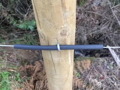 Poste de madera con aislador y cable de cerca eléctrica en campo